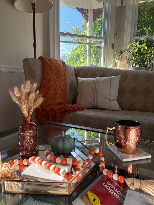 Living room with a couch, coffee table, and fall decorations including a vase with pampass grass, green pumpkin, coasters, and wooden beaded tassel.