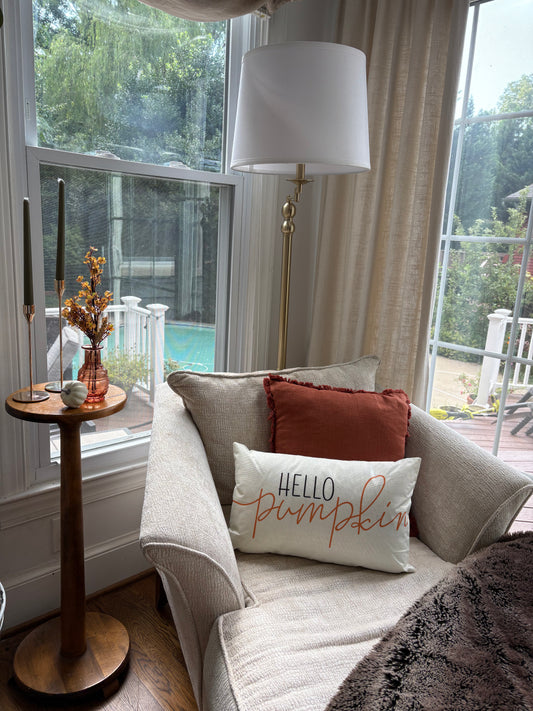 Cozy fall living room with a sofa, lamp, decorative pillows, and a small side table with candlesticks, a vase with flowers, and pumpkins.