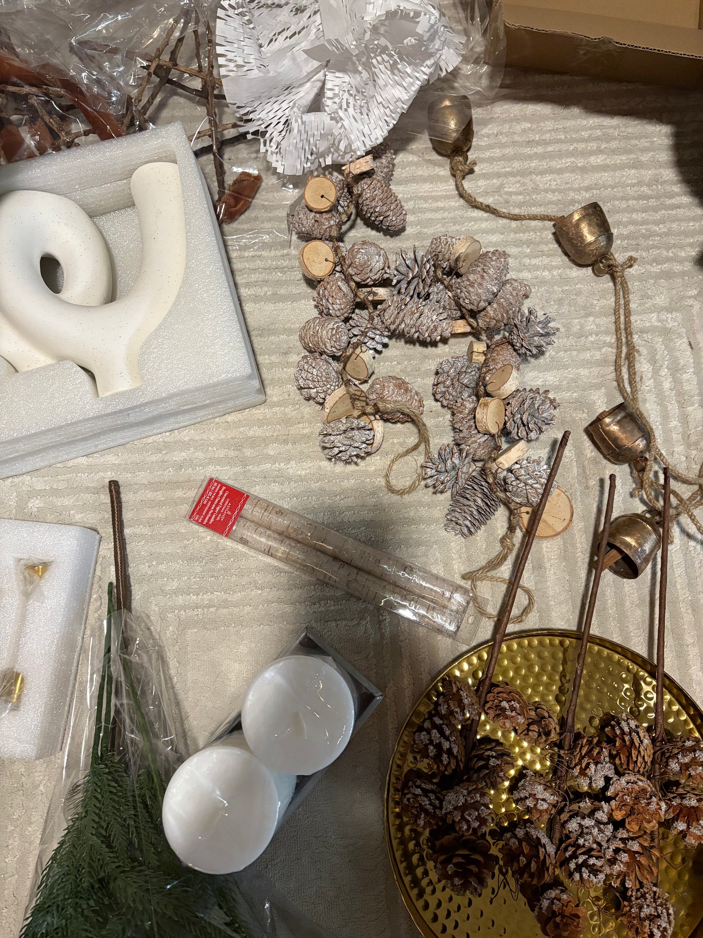 Decorative items including candles, pinecones, and a gold plate on a textured surface.