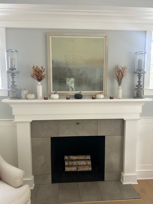 Decorative fireplace mantel with candles, vases, pumpkins, and a painting.