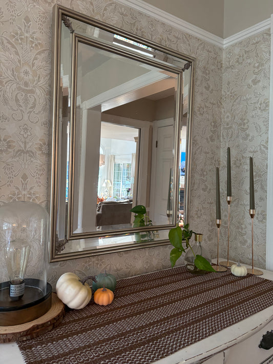 Decorative fall setup with a large mirror, candles, and pumpkins on a table.