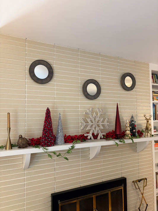 Mantel with Christmas decorations including snowflake, colorful trees, and garlands against a beige wall.