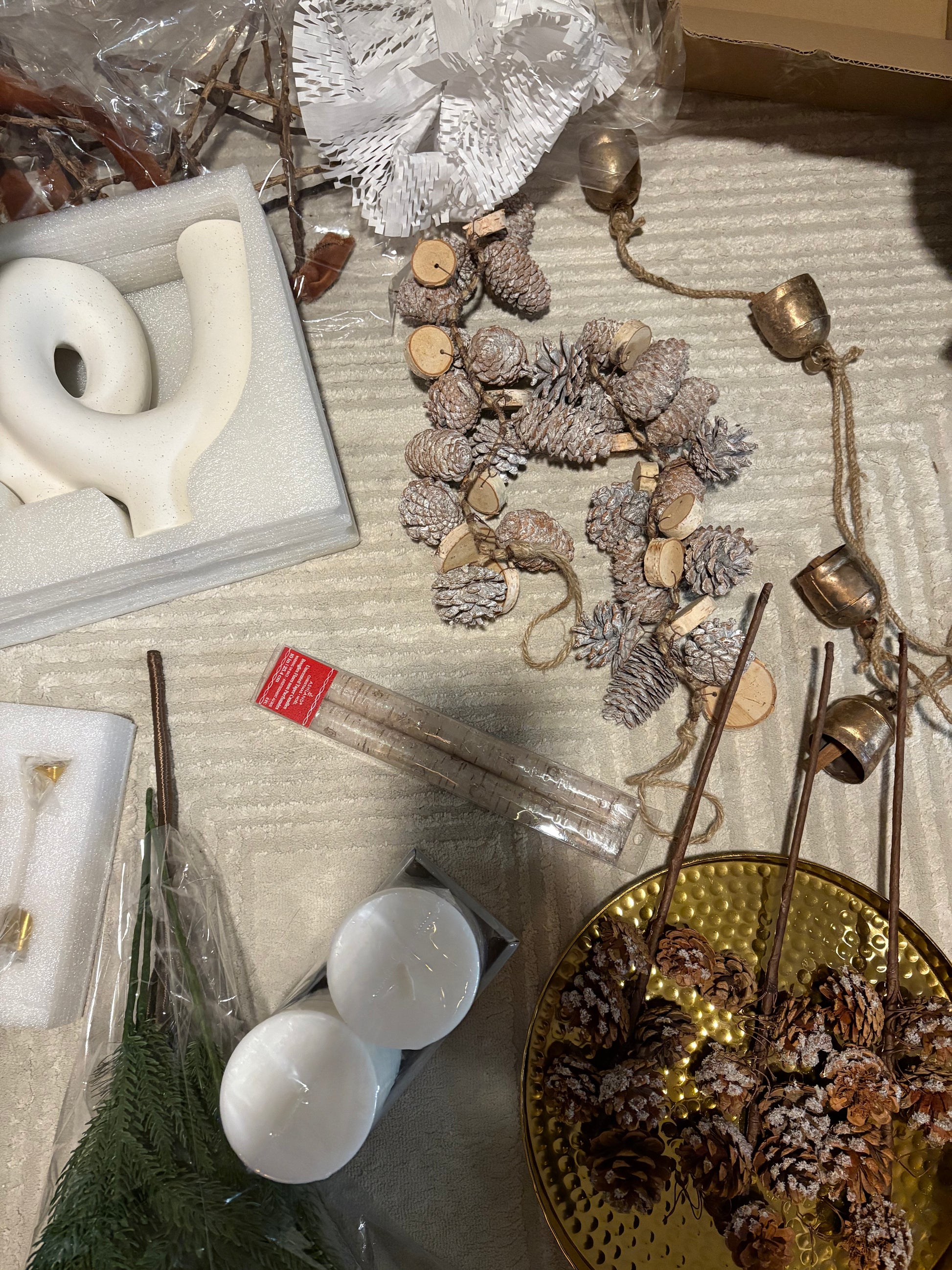 Decorative items including candles, pinecones, and a gold plate on a textured surface.