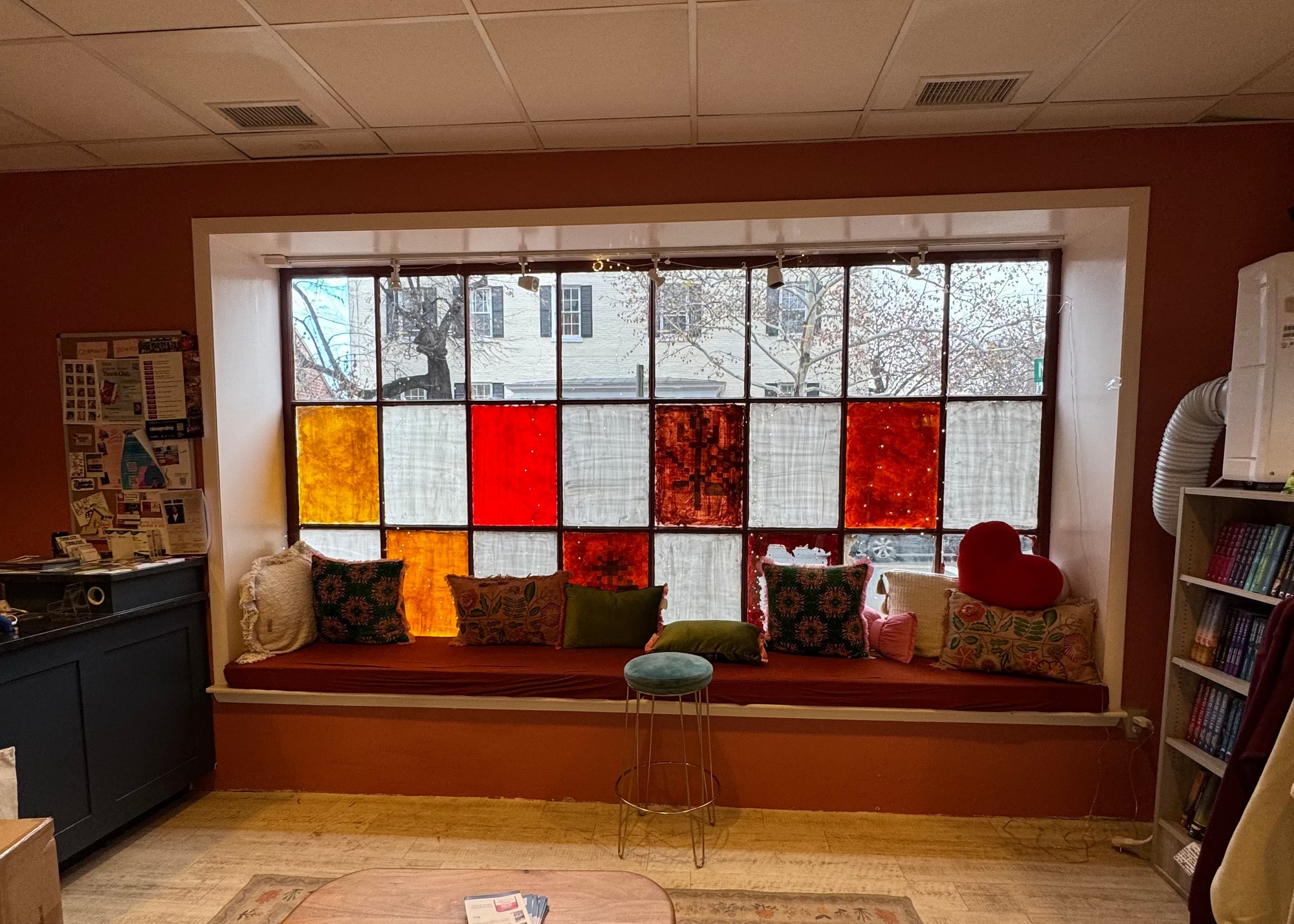 Room interior with a colorful stained glass window, bookshelf, and seating area.