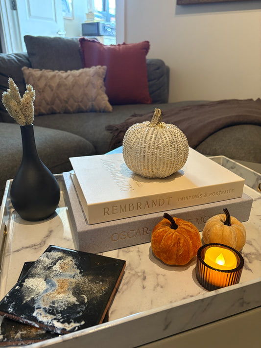 Decorative fall setup on a coffee table with pumpkins, a candle, and books in a living room.