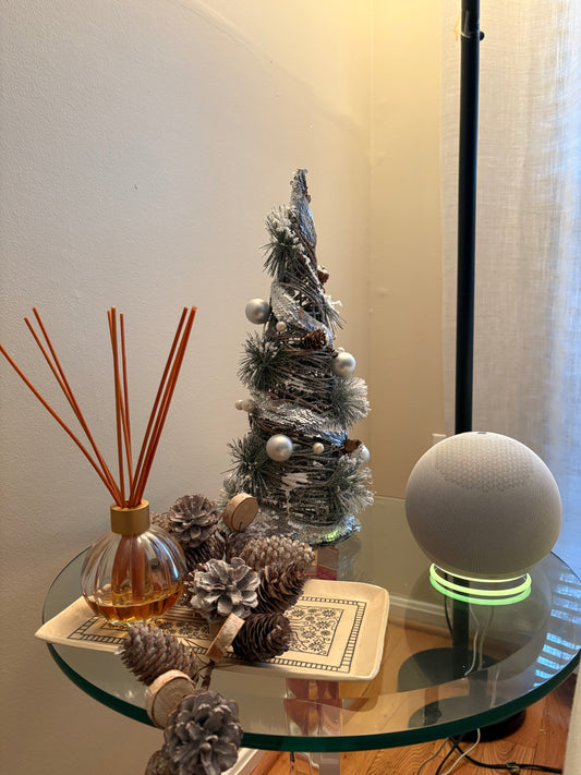 Decorative items on a glass table including a small Christmas tree, diffuser, and decorative pinecones.