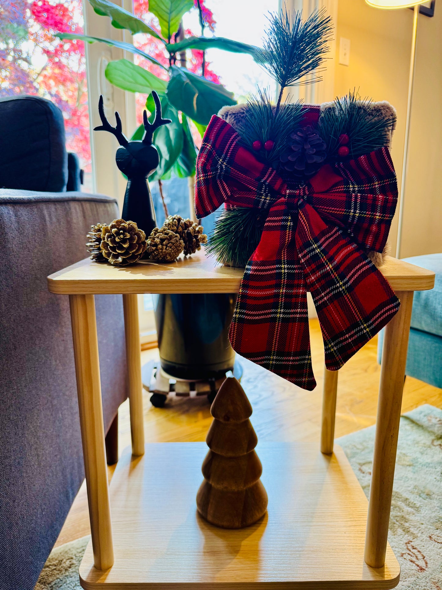 Decorative plaid present with bow and pinecones on a small wooden table in a cozy room.