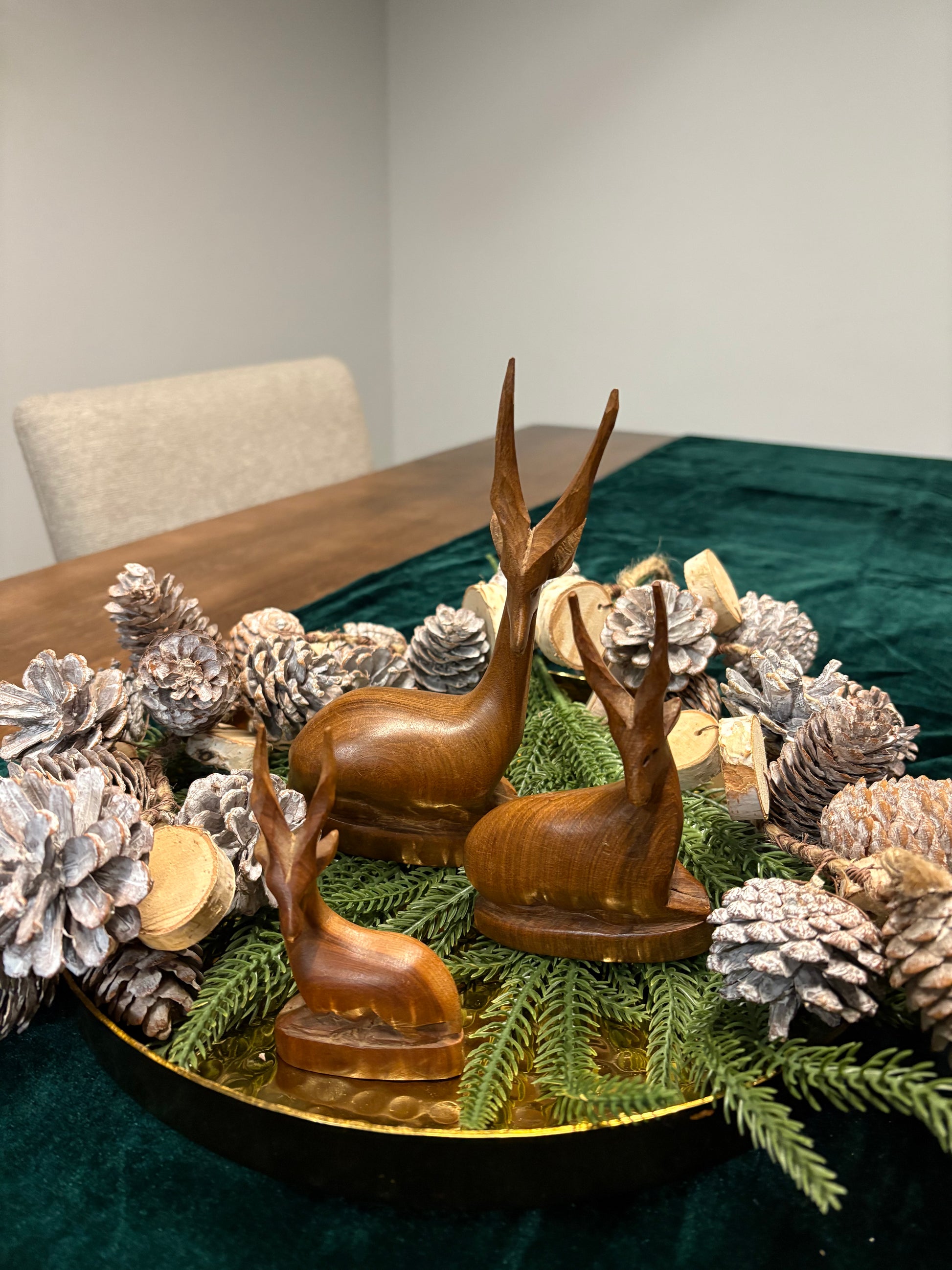 Wooden deer figurines on a table with decorative pinecones and greenery