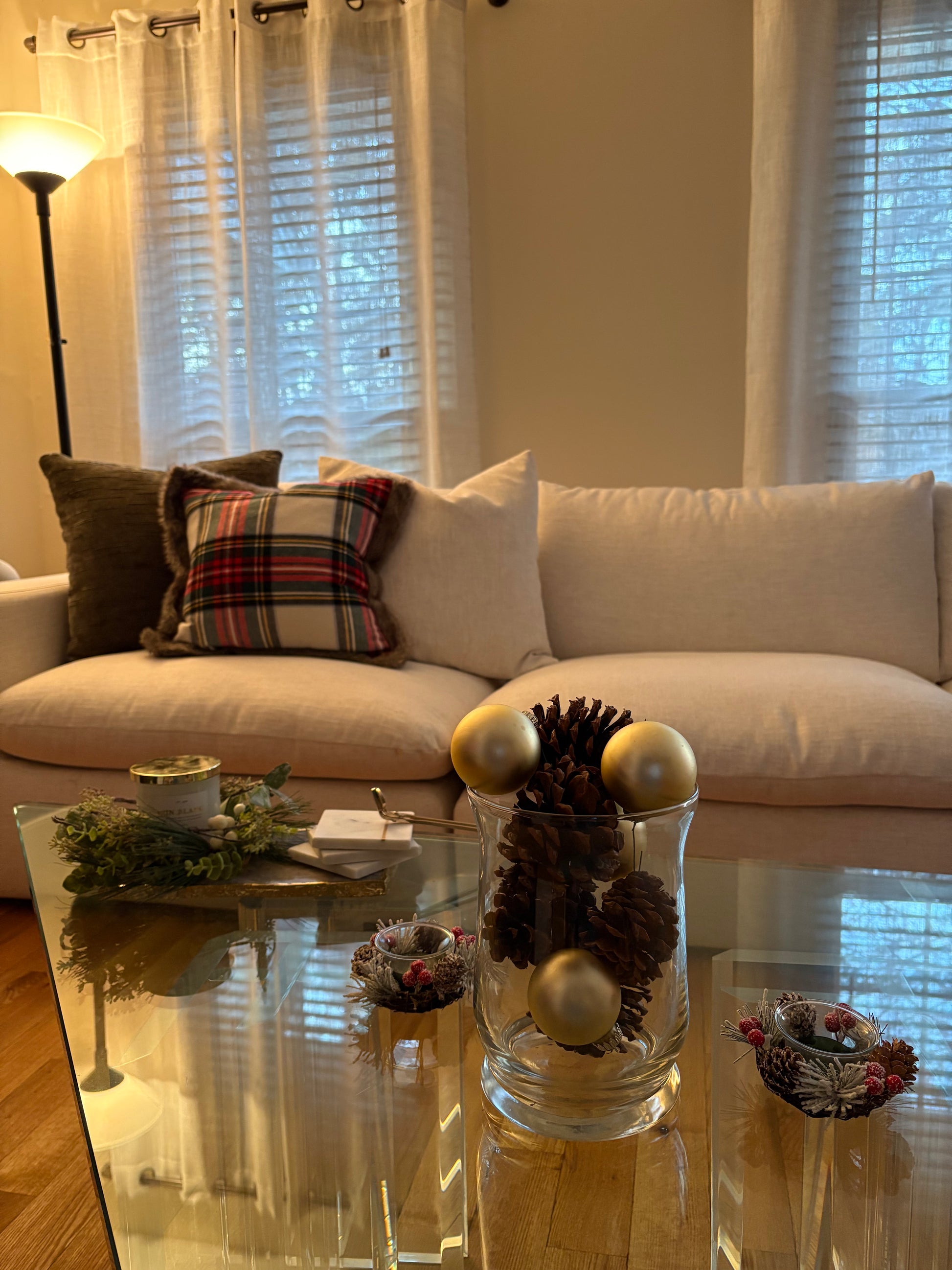 Living room decorated for winter with a white sofa, decorative Christmas pillows, pinecones and ornaments in a glass bowl on glass coffee table.