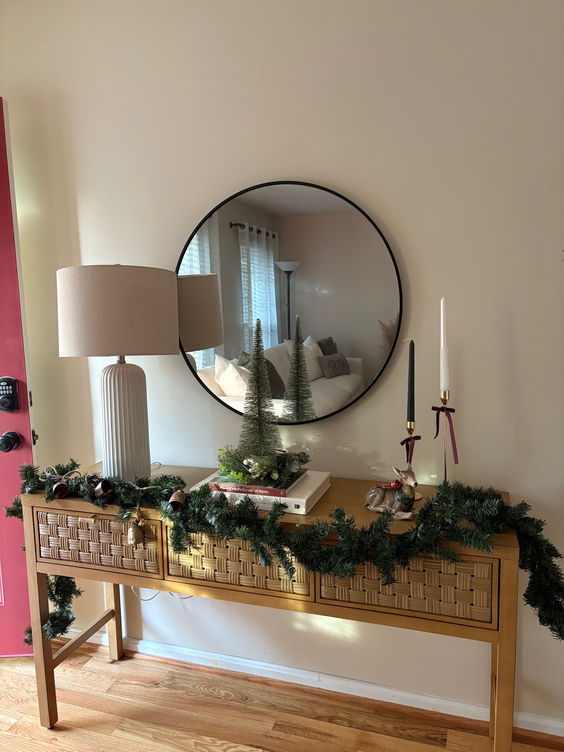 Decorative winter console table with festive garland, candles, and a mirror on a wall.