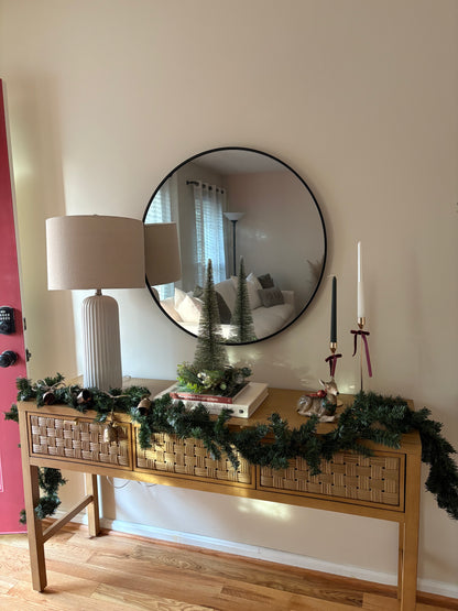 Decorative winter console table with festive garland, candles, and a mirror on a wall.