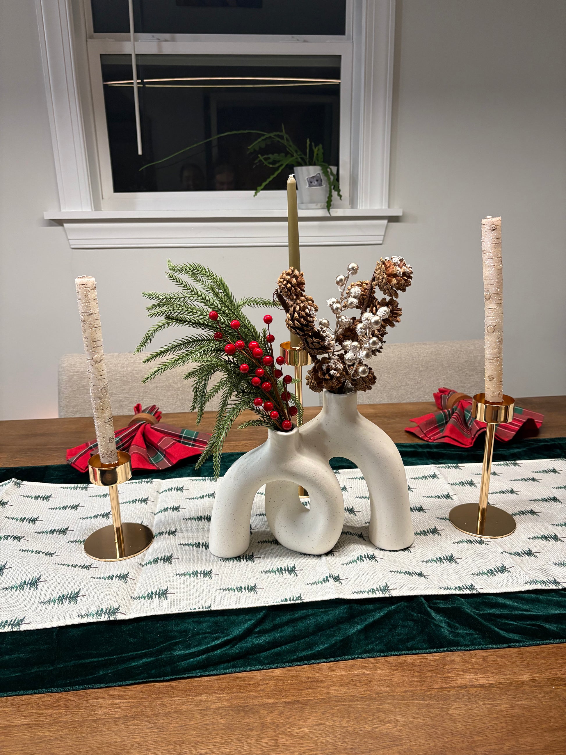 Decorative table setting with a vase of greenery, berries, and pinecones on a tablecloth.