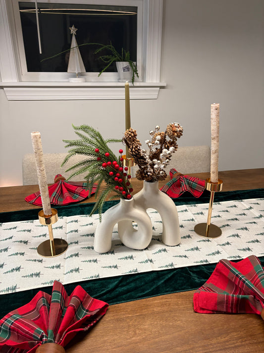 Decorative table setting with candles, greenery, and plaid napkins on a festive winter tablecloth.