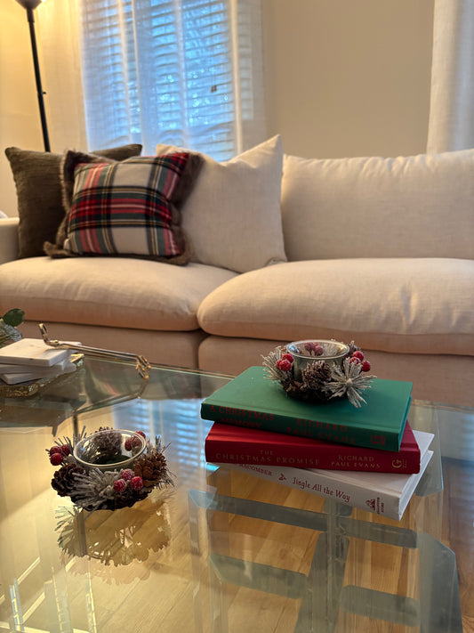 Living room decorated for winter with a beige sofa, plaid pillow, and Christmas books on a glass coffee table.