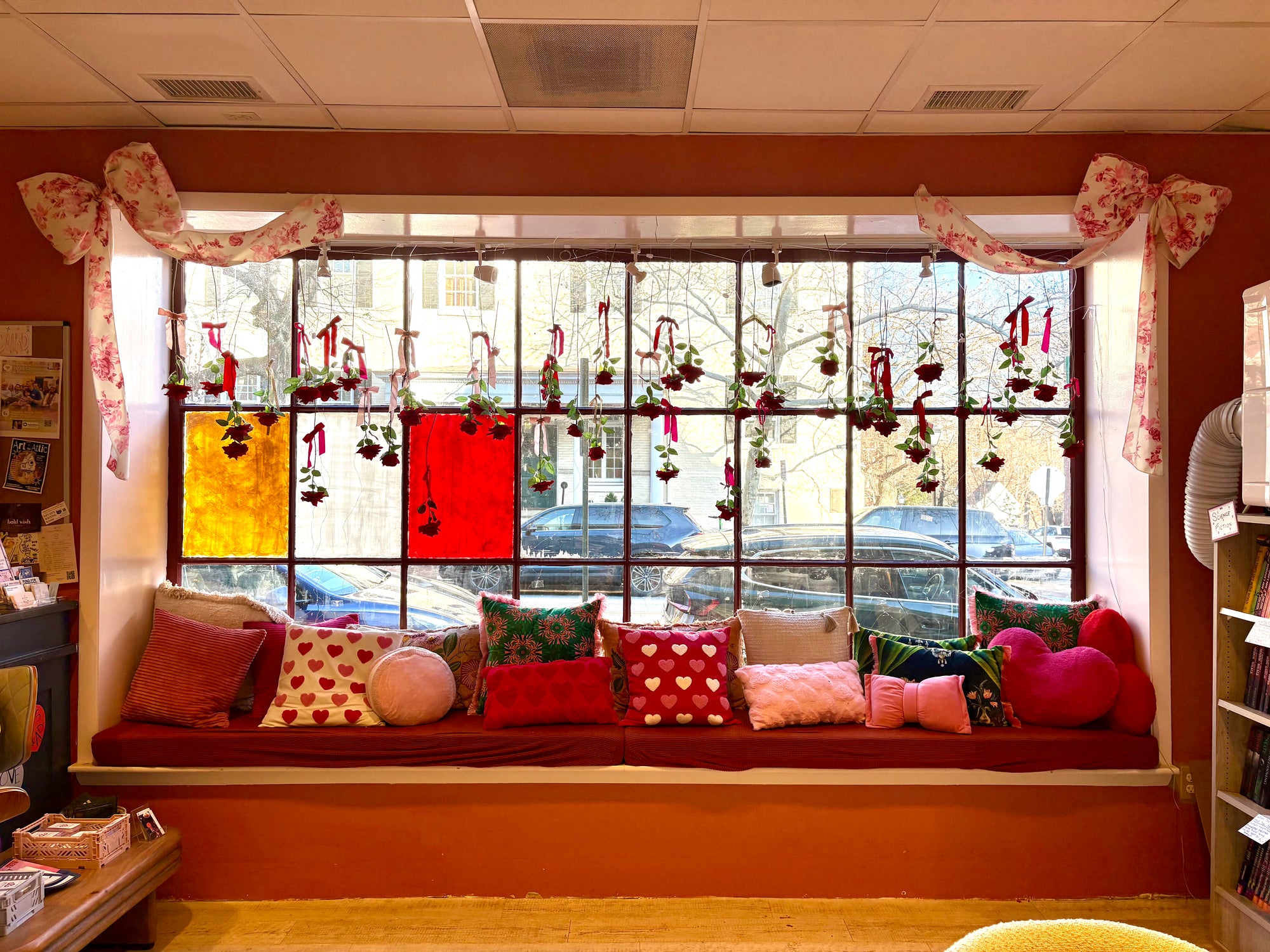 Window seat in Friends to Lovers, a romance bookstore in Old Town Alexandria, decorated for Valentine's Day with rental decor including hanging roses, big floral bows, and pink and red heart pillows pillows.