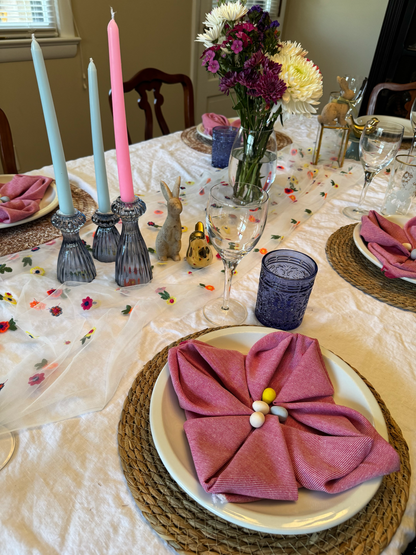 Dining table set for Easter with rental decor including pink napkins, candles in glass candle holders, bunny and bird figurines, and a table runner with flowers.