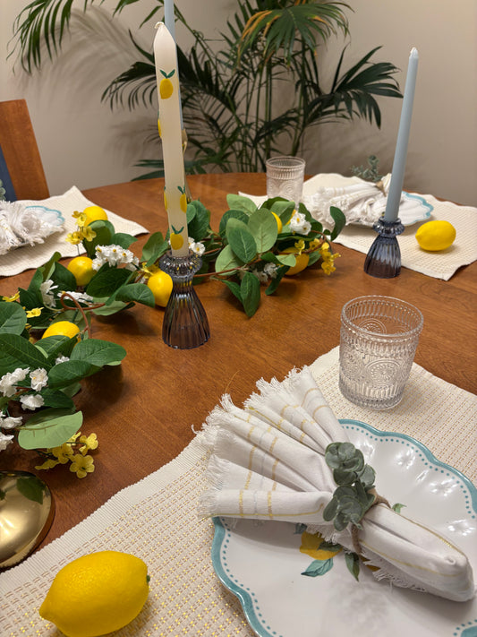 Close up of a table setting with rental decor including lemons, candles, and greenery on a wooden table.