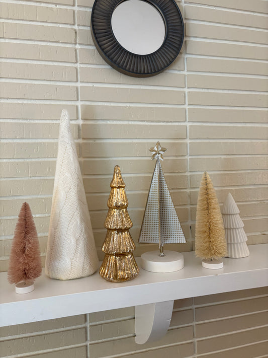 Decorative white and gold Christmas trees on a shelf against a tiled wall.